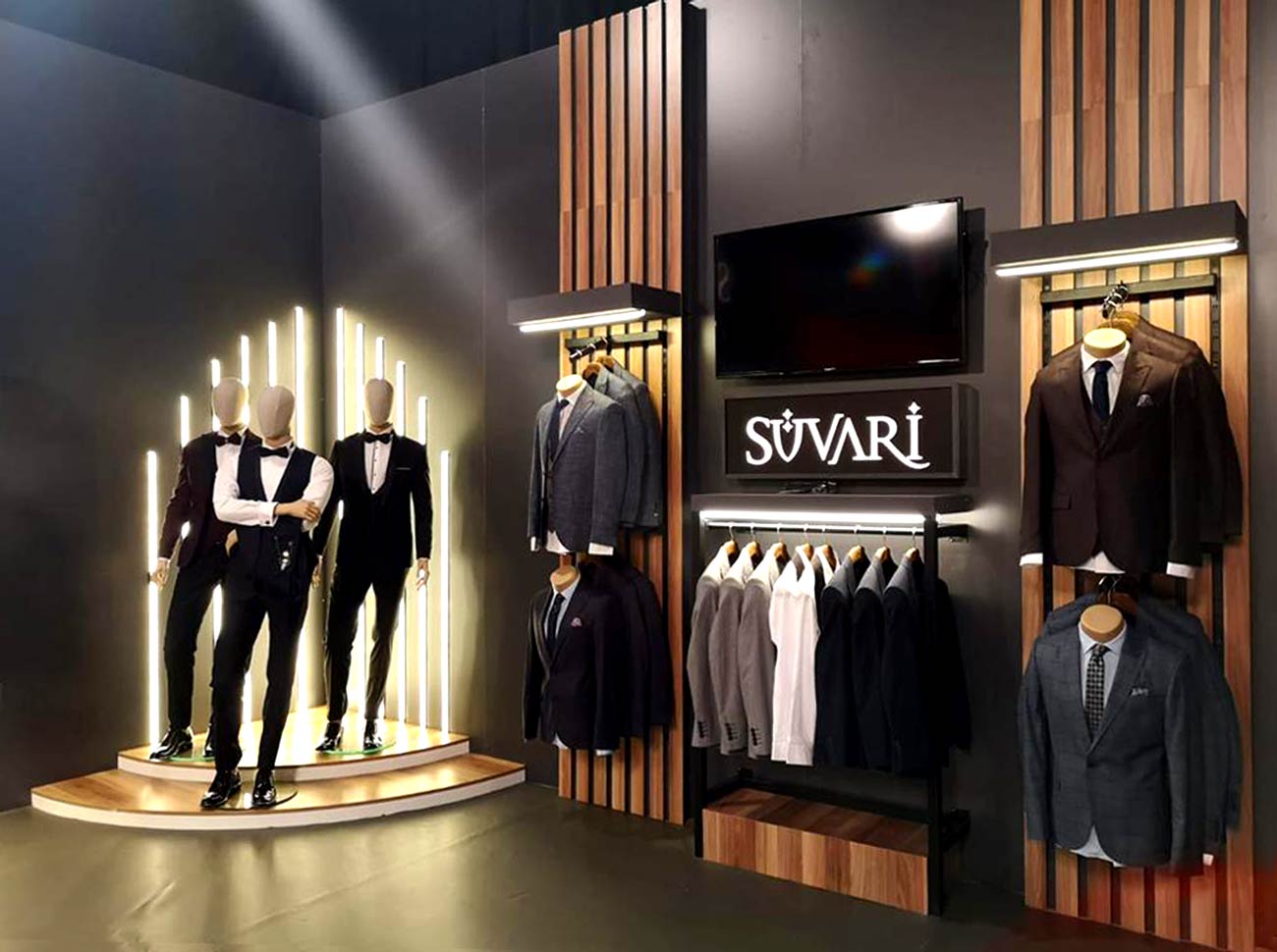 Corner of Suvari Trade Stand showroom in black background. Suit clothing hung on the wall in front and between.