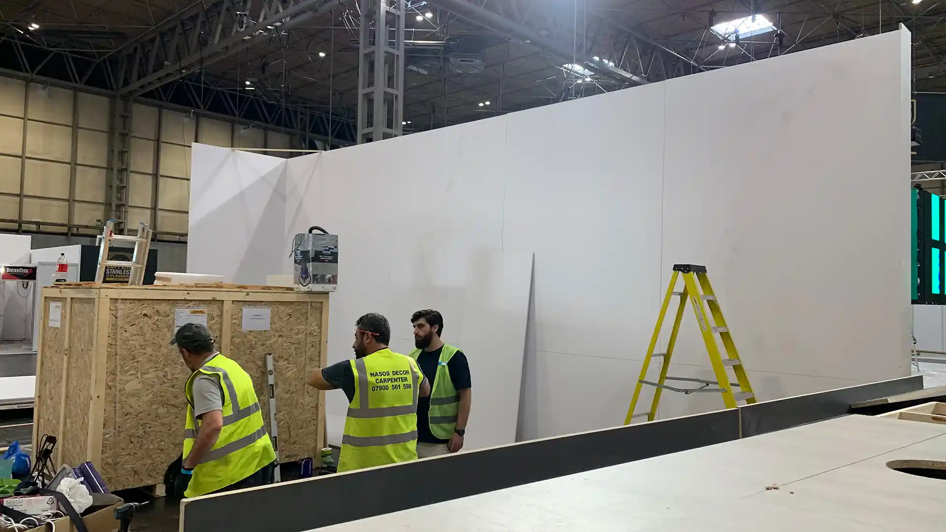 White trade stand construction with three man standing wearing hi viz vests