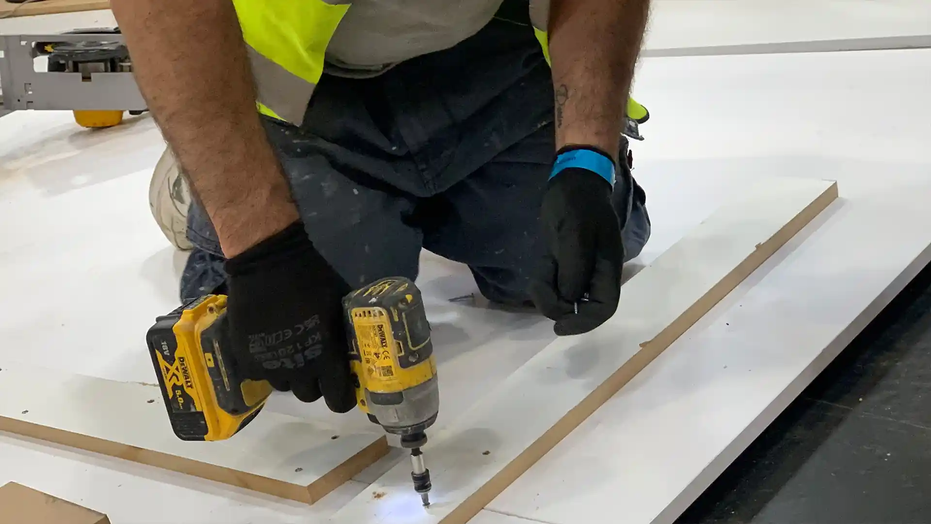 Construction worker using drill on white MDF wearing hi viz vest